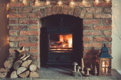 Log burner fireplace with burning logs, handmade wooden toys, lantern and logs around, selective focus; dark vintage style toned photo